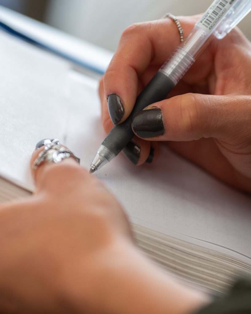 A person holds a pen and is writing in a notebook