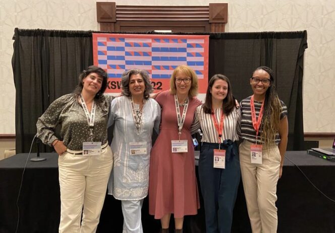 Elise poses with four members of CJRF team. Behind them is a table in front of a black curtain and patterned sign.