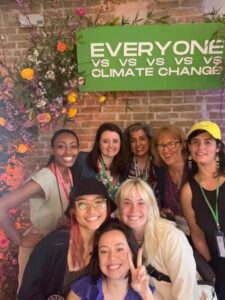 Elise and seven others pose in front of a brick wall, flowers, and a sign that reads "EVERYONE VS VS VS VS CLIMATE CHANGE"