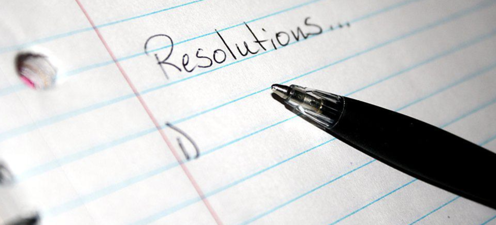 A pen hovers over notebook paper that reads "Resolutions..."