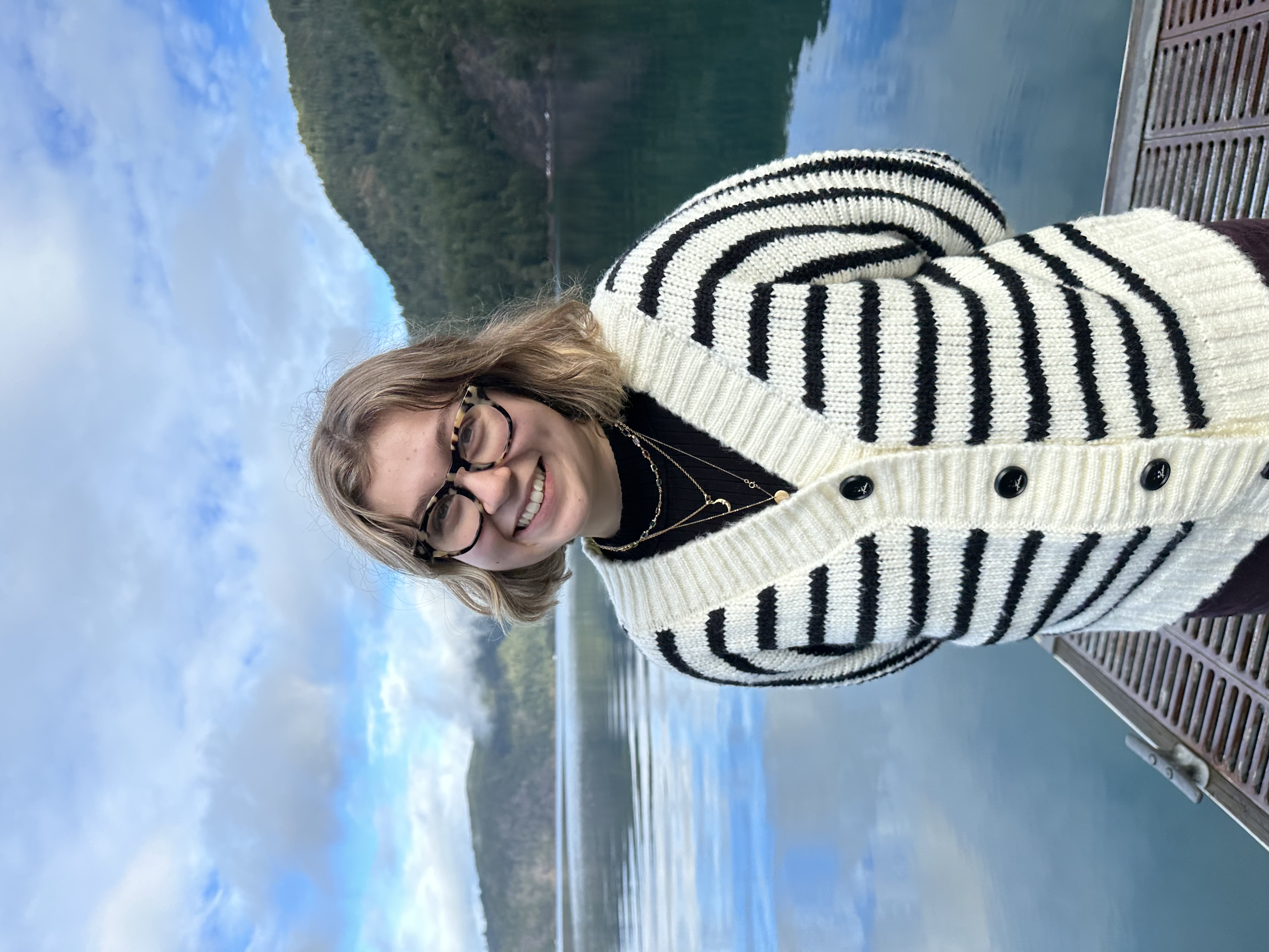 Caroline smiles. In the background, a lake and mountains are visible.
