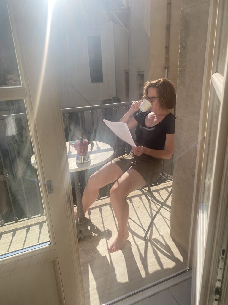 Joy sits on a balcony, drinking espresso and reading a document.