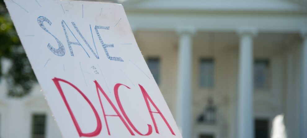 A sign that reads "Save DACA" in blue and red lettering in front of the White House.