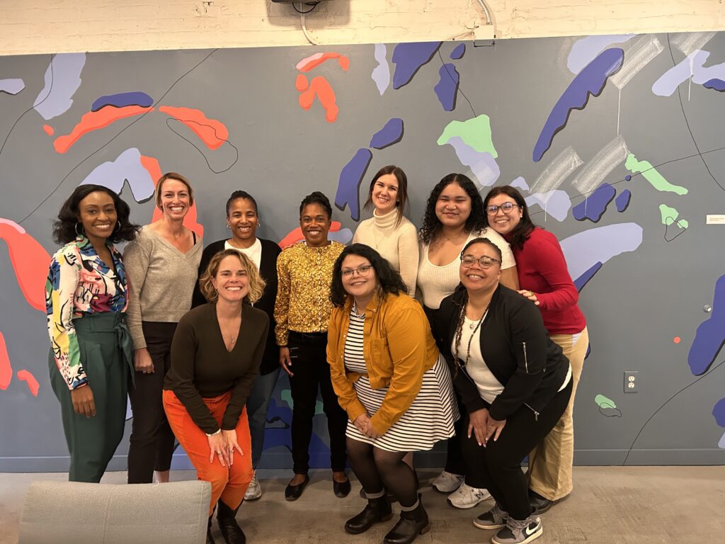 Elise, Sara, Dori, Clothilde, Kayla, Falisha, Caroline, Joy, Gaby, and Crystal smile in front of a colorful background wall.