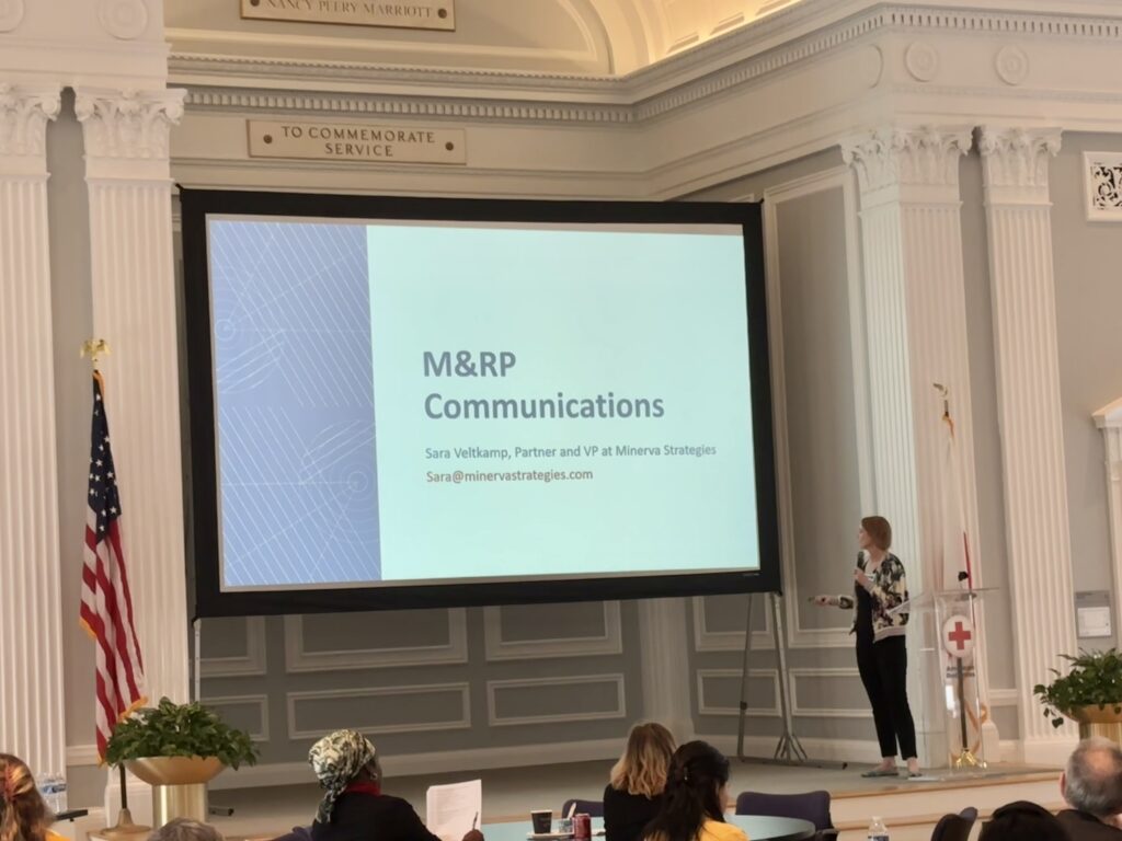 Sara stands on a stage and presents slides that read "M&RP Communications"