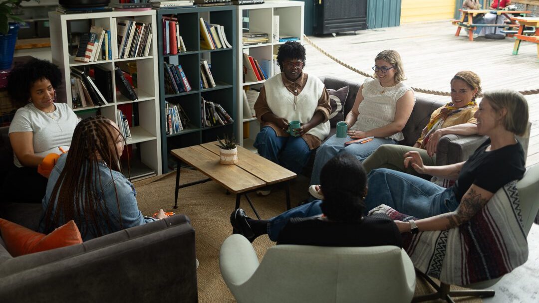 A group of Minerva Strategies team members sit on lounge furniture around a coffee table in a modern office setting. They are having a discussion.