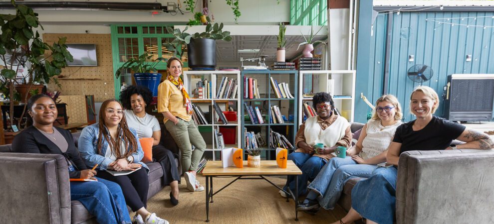 The Minerva team sits and stands in a semi circle at CreateATL, a bright and open coworking space.