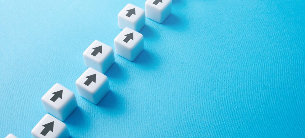 Dice with arrows pointing up stack staggered in a line against a blue background.
