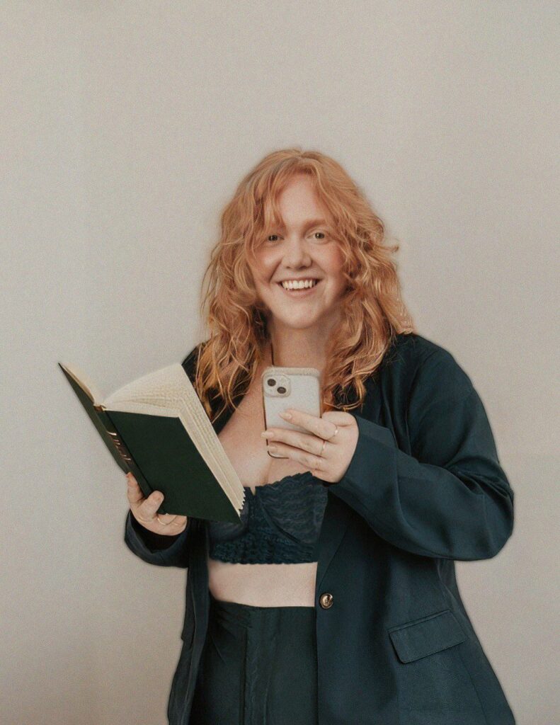 Bailey is a white woman holding a phone and a book, smiling at the camera.