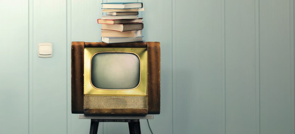 A stack of books sits on top of a vintage tv