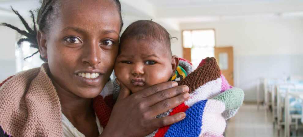 A woman holds a small baby in a maternity ward and squeezes his chubby cheeks.